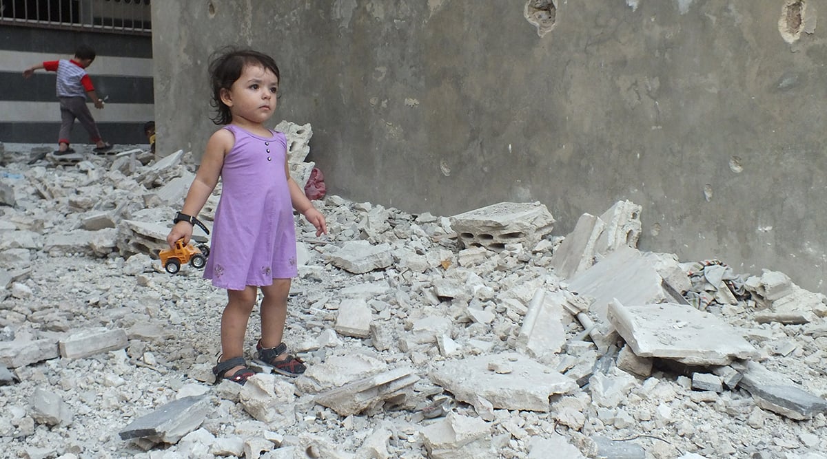 A girl stands on debris next to a damaged building at a besieged area of Homs