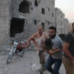 Residents rescue injured child after strike on the displacement center in Hass on August 16, 2019. © MacroMedia Center 2019