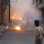 At least four incendiary submunitions burn on the ground of a narrow street in the al-Mashhad neighborhood